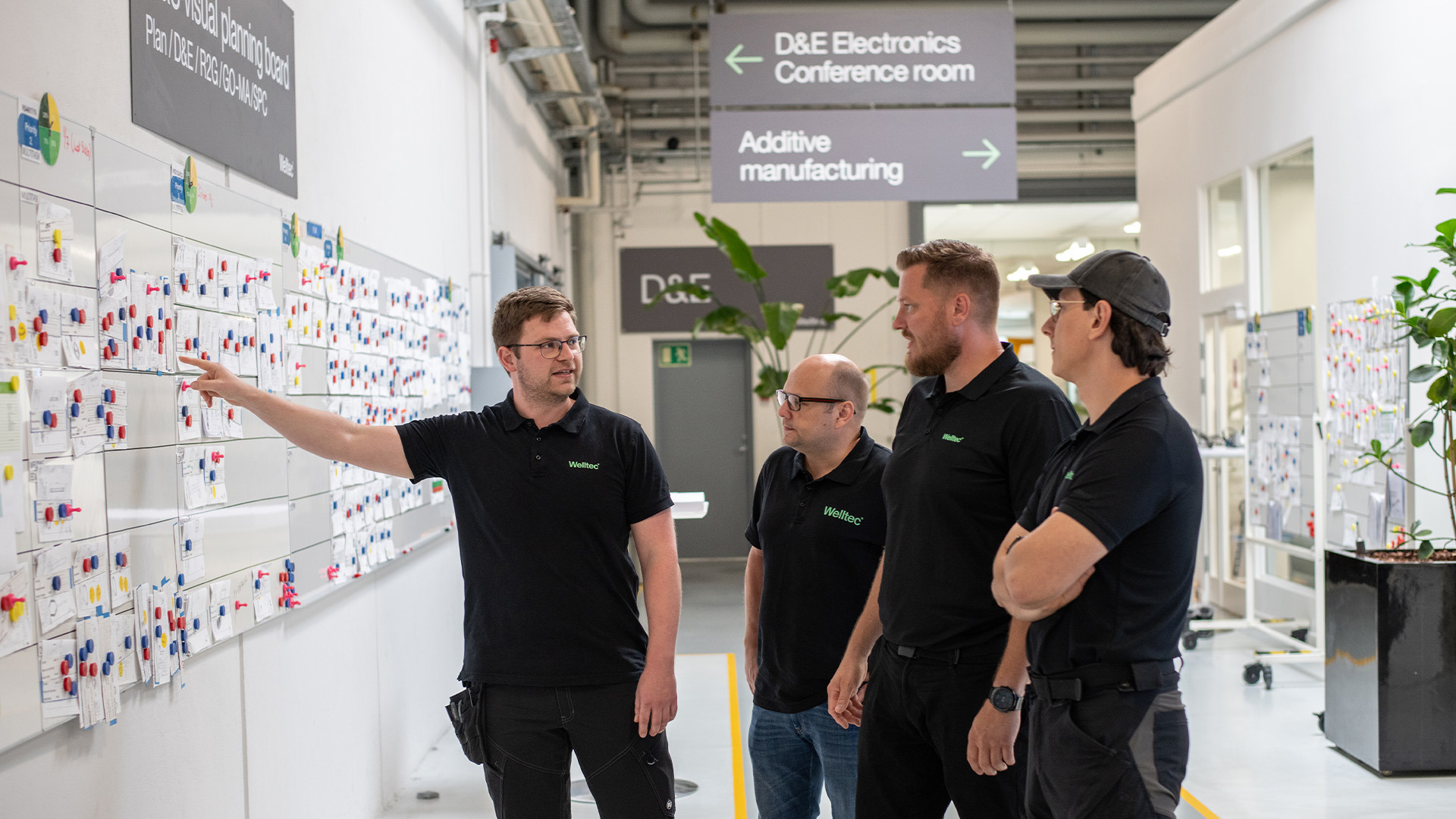 Engineers at Welltec discuss project planning while reviewing a detailed board in a modern office hallway.