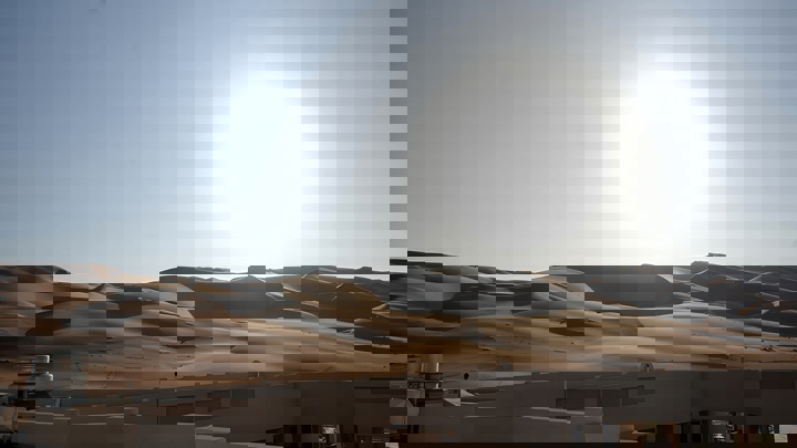 Sunrise over desert sand dunes with building rooftops in the foreground