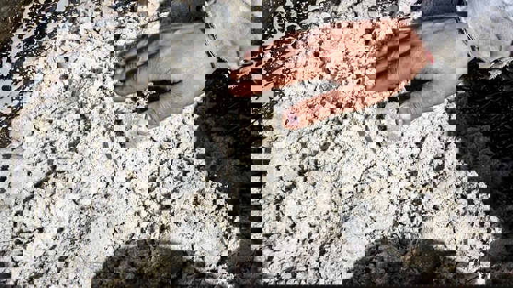 Hand touching chalky debris from wellbore, showing scale and texture of removed formation.