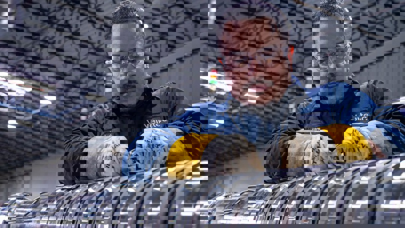 Welltec engineer wearing protective gear and gloves, working with precision metal components in a manufacturing facility.