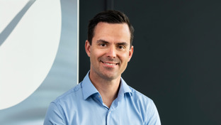 Petter Lønning, Sales Director, standing against a dark background wearing a blue shirt and smiling.
